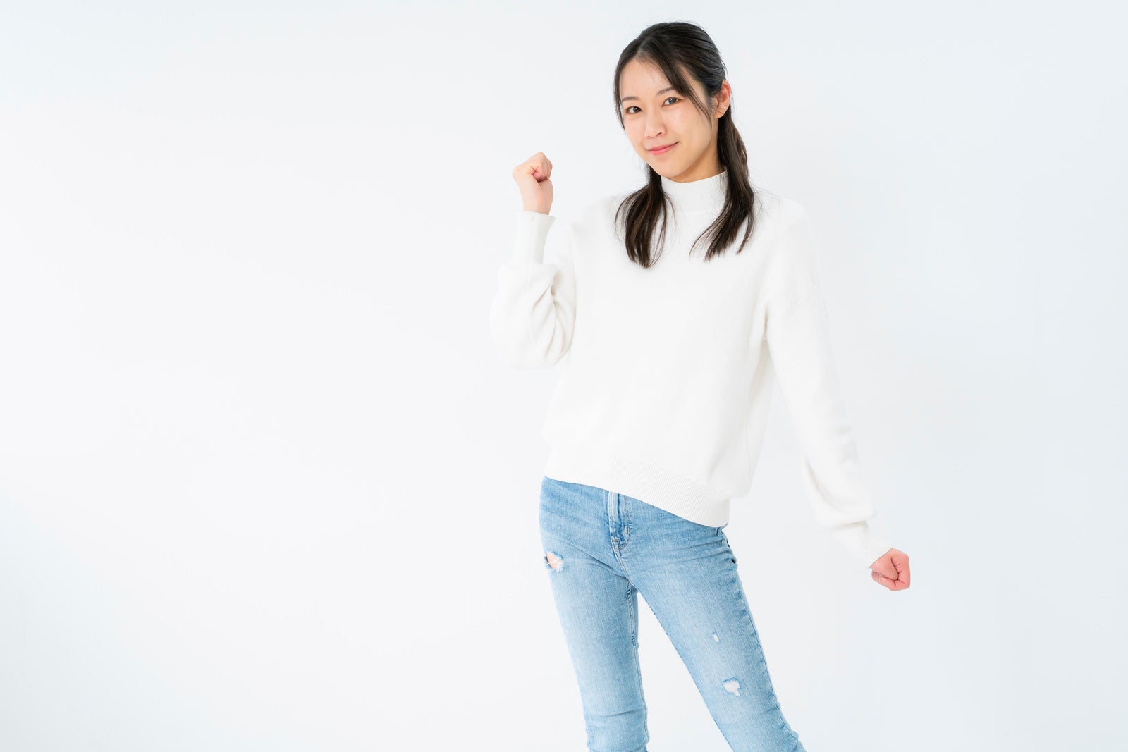 白背景で両手を握りガッツポーズをとりながら微笑む白ニットの女性［モデル：SAKI］
