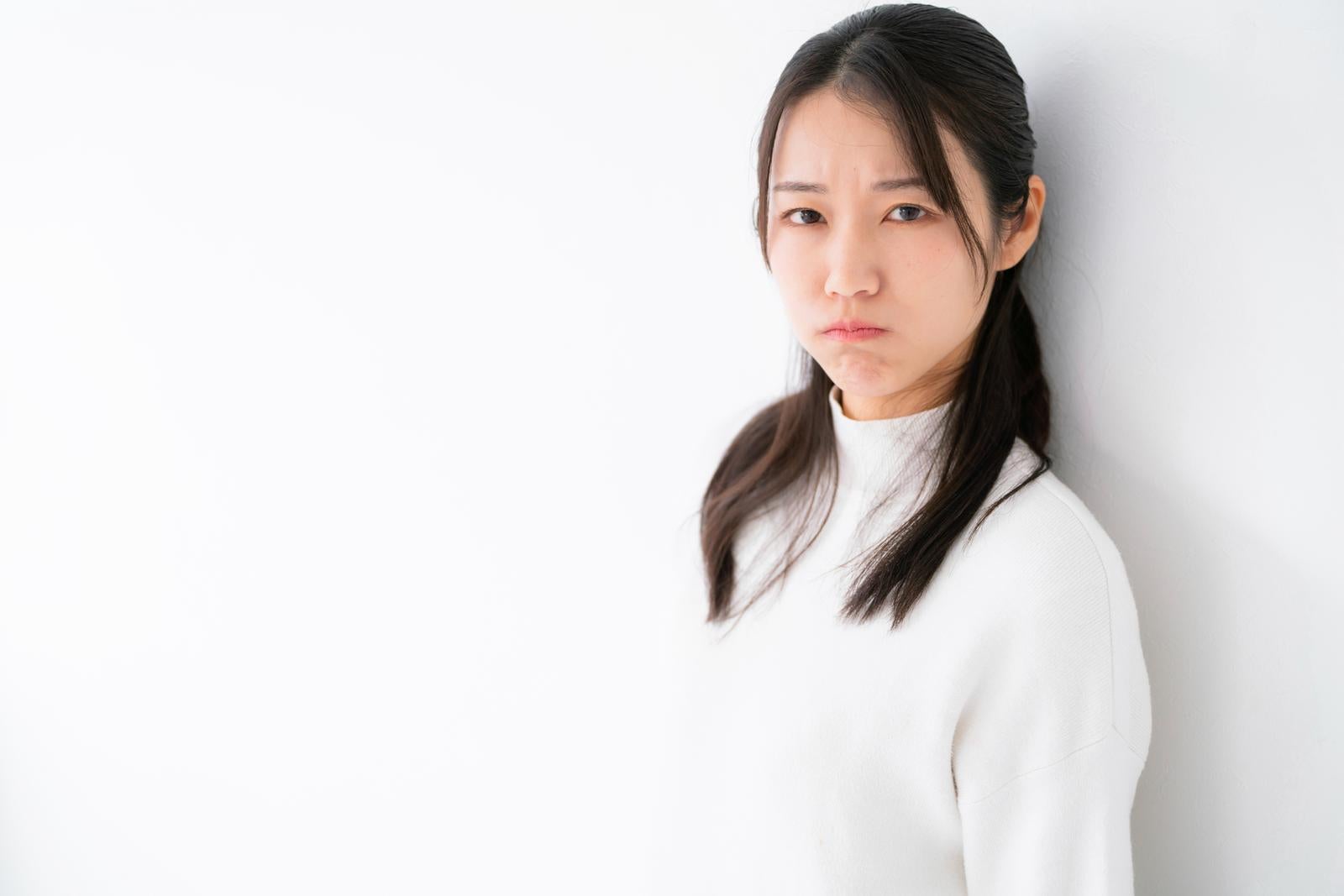 「拗ねた表情で壁にもたれる女性」の写真［モデル：SAKI］