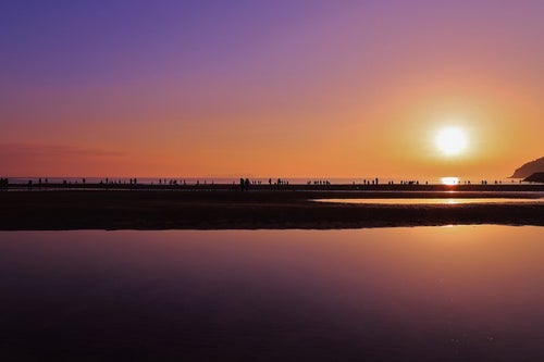沈む夕日と浜辺で遊ぶ人々のシルエットの写真