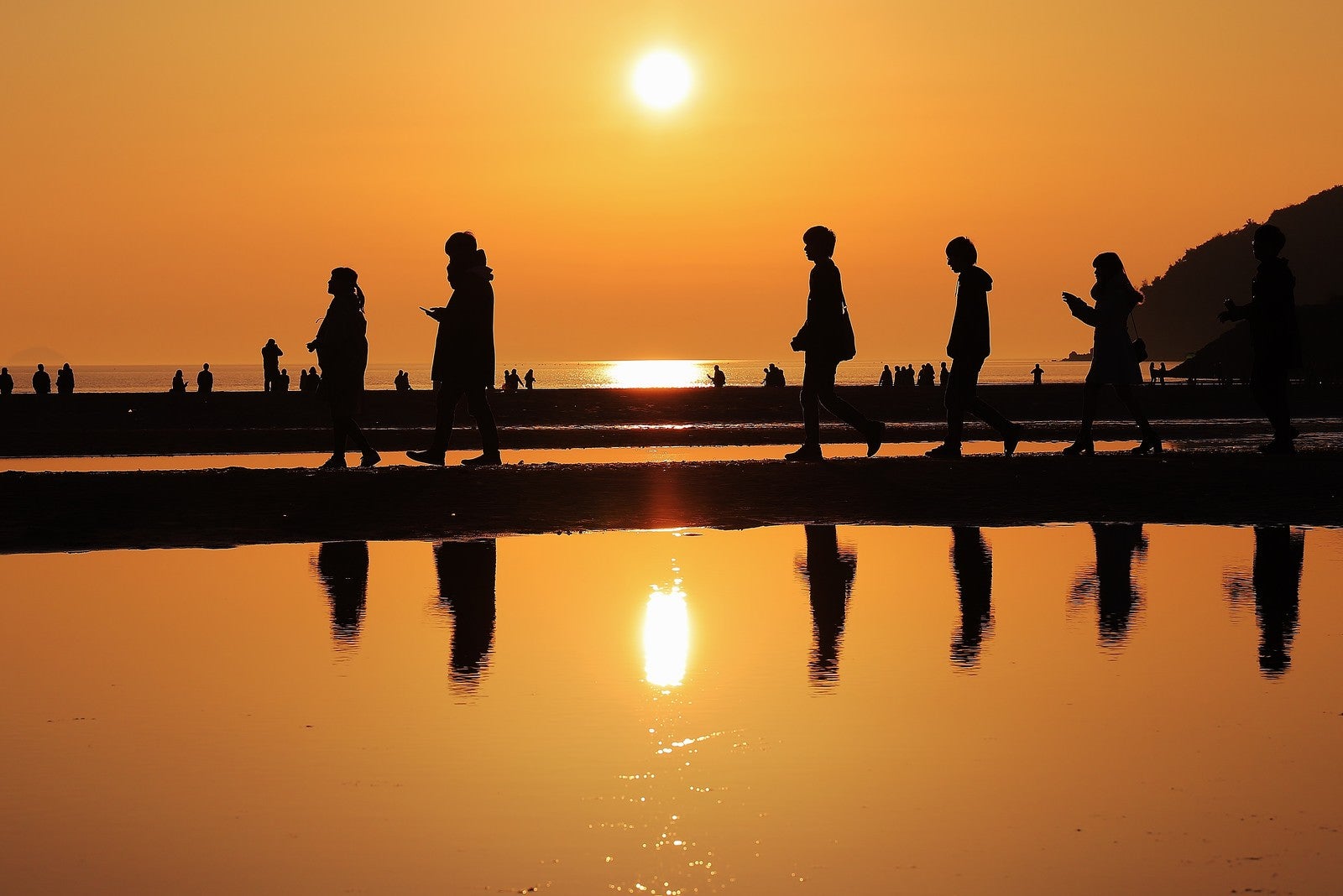「夕暮れ時に砂浜を散策する人達のシルエット」の写真