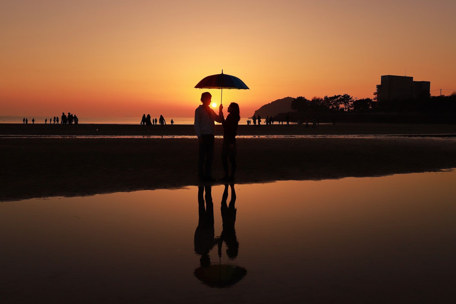 「夕暮れ時に浜辺で相合傘するカップル」の写真