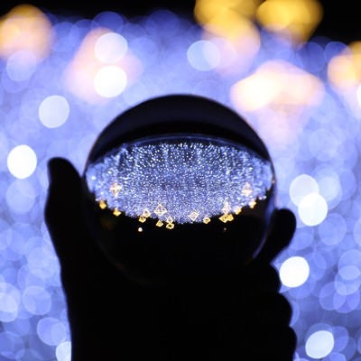 手に持つガラス玉に写り込むイルミネーション（神戸ルミナリエ）の写真