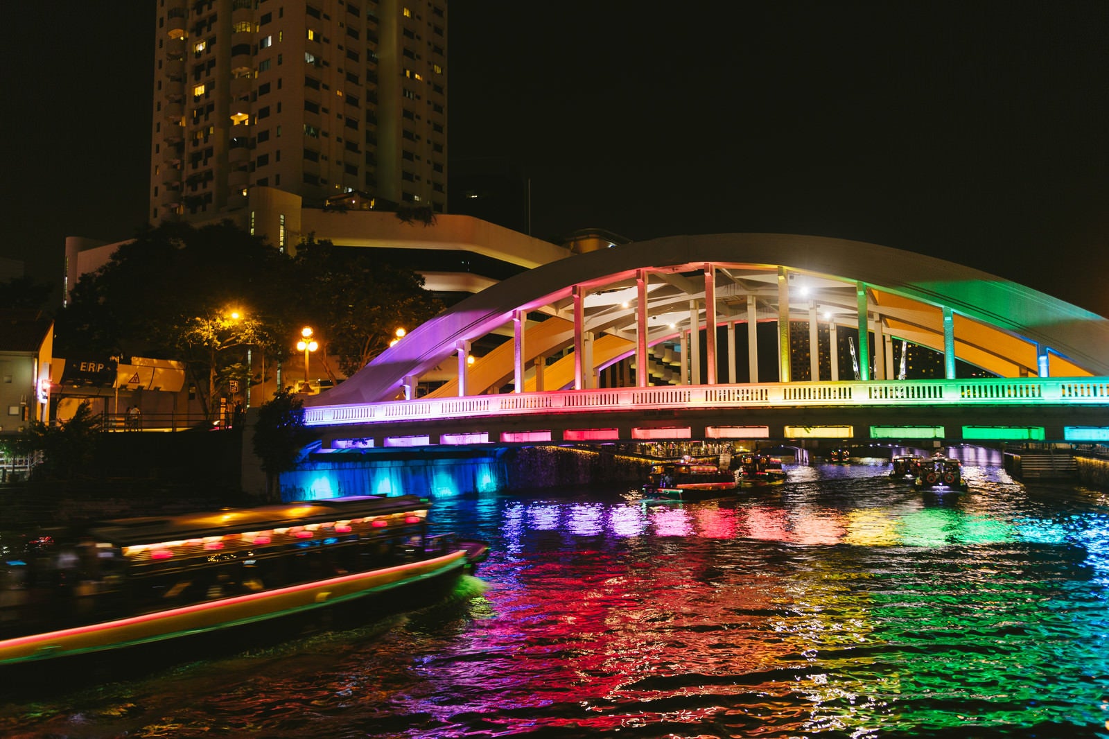 「虹色にライトアップされた橋と屋形船（シンガポール）」の写真