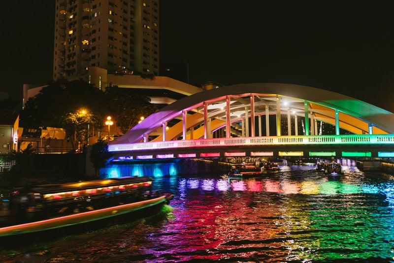 虹色にライトアップされた橋と屋形船（シンガポール）の写真