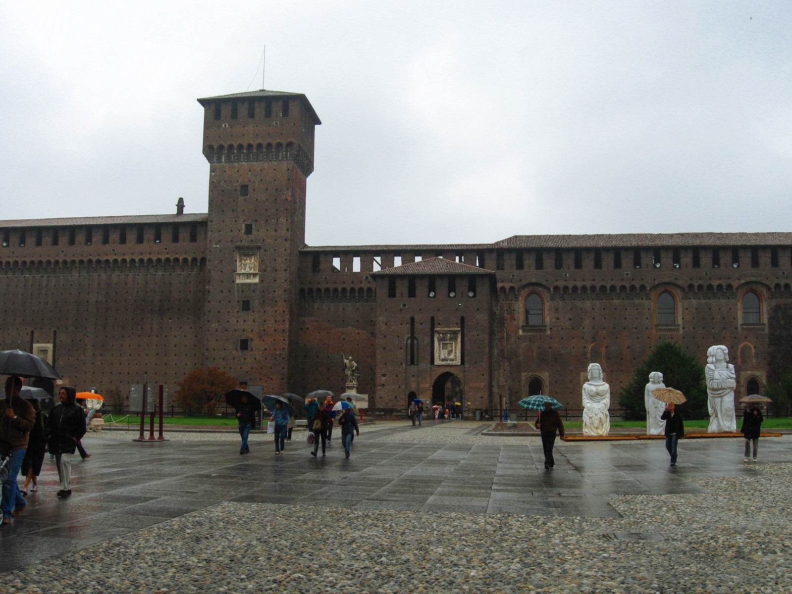 「スフォルツェスコ城前の広場を行き交う傘を差す観光客（イタリア ミラノ）」の写真