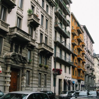 ミラノの通りを行き交う車と通りに面した建造物（イタリア）の写真