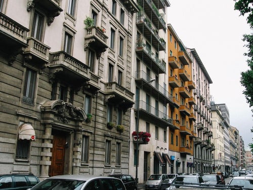 ミラノの通りを行き交う車と通りに面した建造物（イタリア）の写真