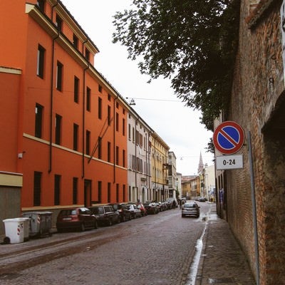 マントヴァの街角に駐車する車とレンガ造りの壁前に立つ標識（イタリア）の写真