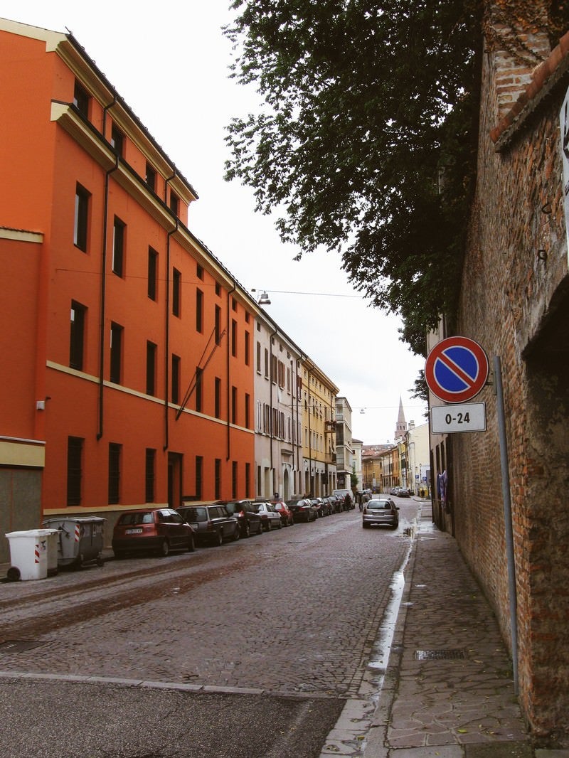 「マントヴァの街角に駐車する車とレンガ造りの壁前に立つ標識（イタリア）」の写真