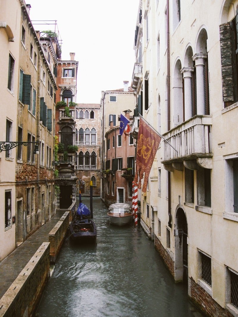 ヴェネツィアの水路に浮かぶ小船と旗が立つ建物（イタリア）の写真