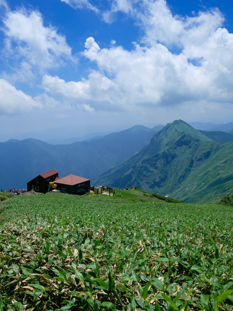 「登山道に現れた山小屋と山峰の風景」の写真