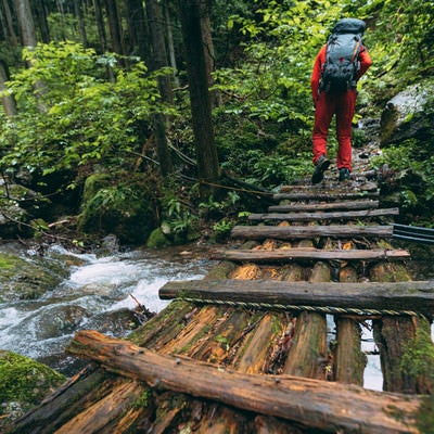 渓流にかかる木製の橋を渡る登山者の写真
