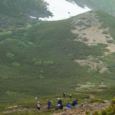 傾斜のある登山道を下山する登山者の列の写真