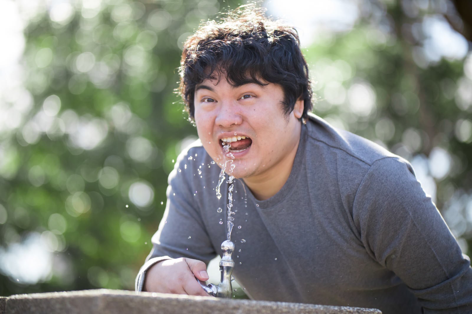 「公園の水飲み場を使う男性」の写真［モデル：段田隼人］