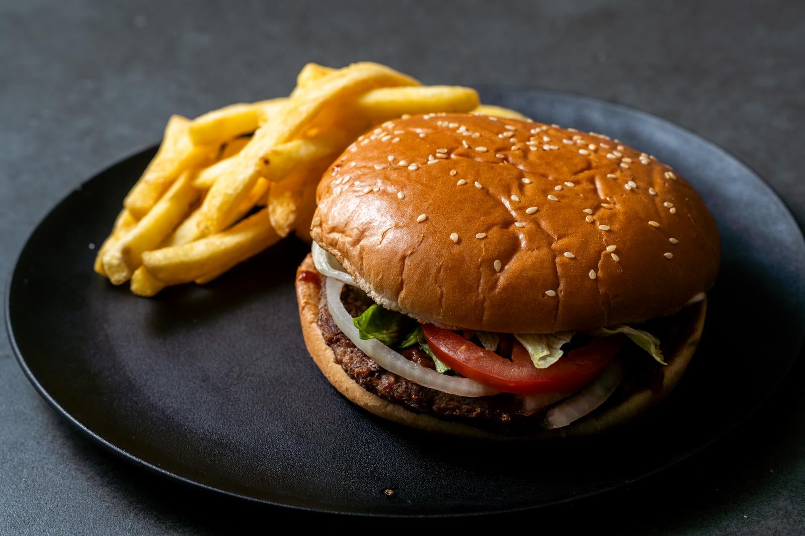 黒い皿に載ったゴマ付きバンズのハンバーガーとフライドポテトのセット