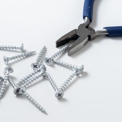 青いハンドルのペンチと散らばったネジの写真