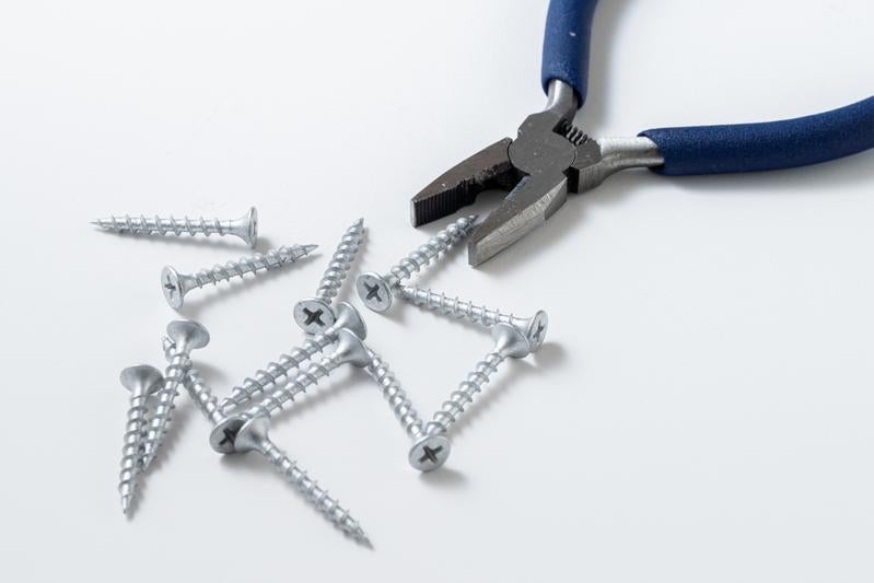 青いハンドルのペンチと散らばったネジの写真