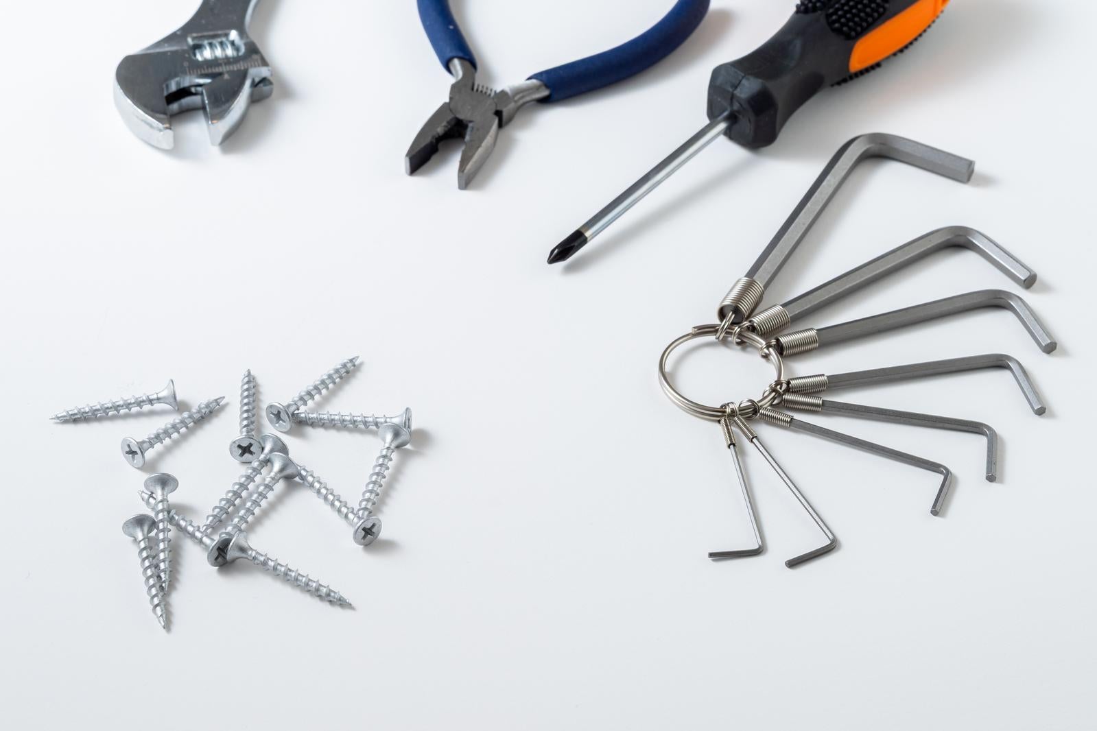 白い背景に配置されたモンキーレンチ、ペンチ、ドライバー、六角レンチセット、ネジなどの工具類