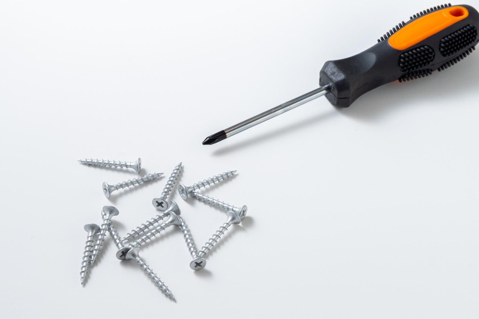 白背景に置かれたオレンジ色のプラスドライバーと複数のシルバー色のネジ