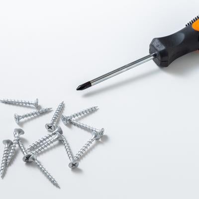 白背景に置かれたオレンジ色のプラスドライバーと散らばったネジの写真