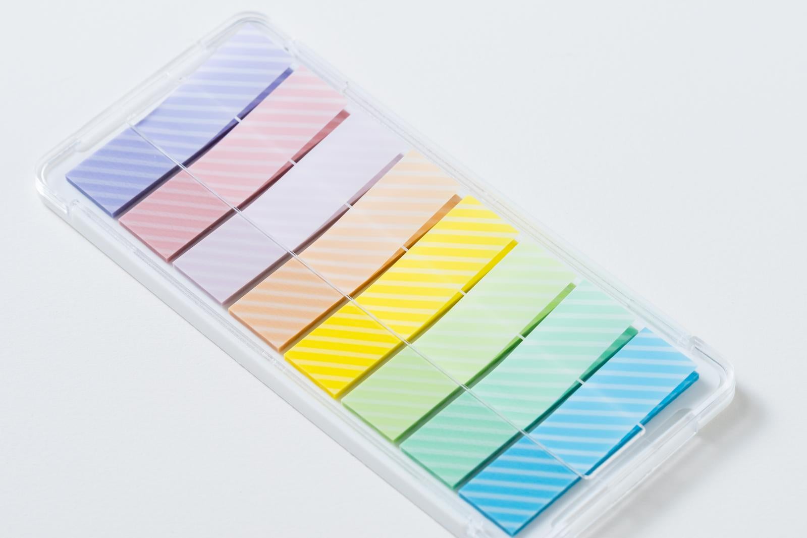 透明プラスチックケースに紫、ピンク、黄、緑、青のレインボーカラーの付箋が整理収納されている