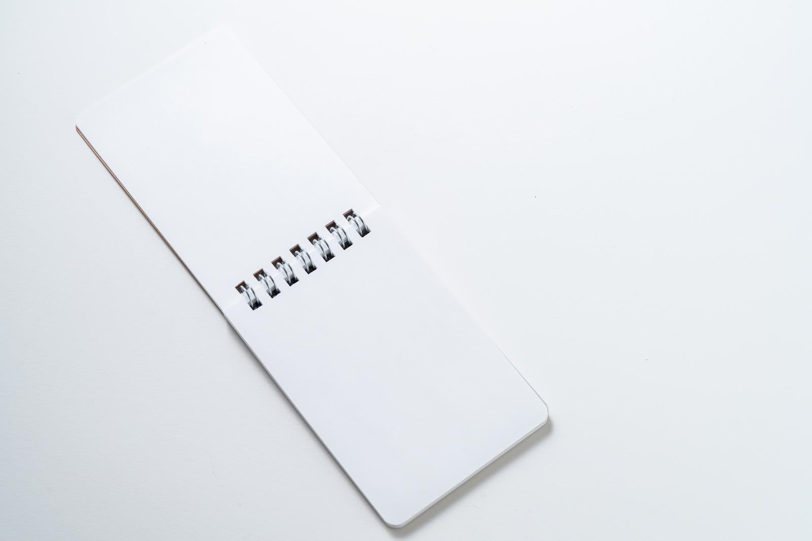 白背景の上に斜めに置かれた白い表紙のリングメモ帳