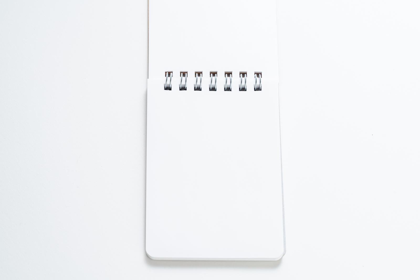 白い背景の上に置かれたリング式の白いメモ帳