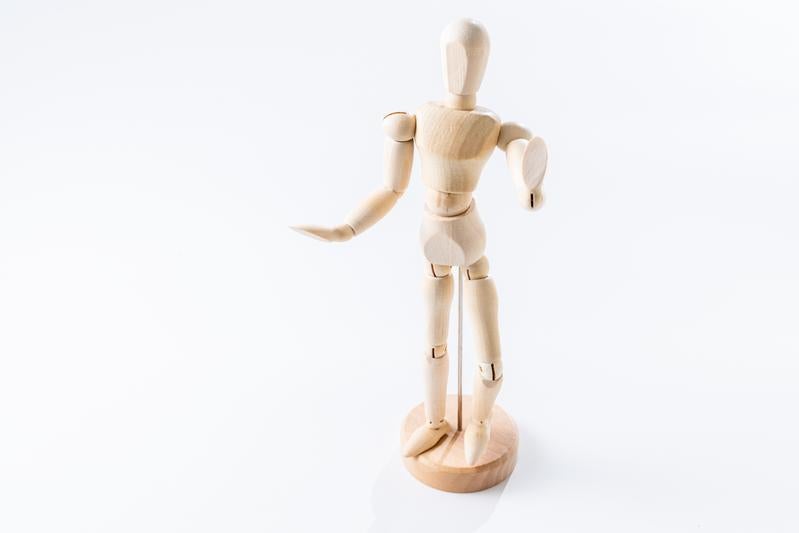 右手を前に伸ばし左手を腰に当てる木製デッサン人形の写真