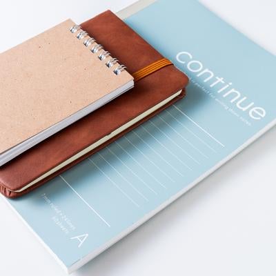 デスクに並べられたリングノートと革製手帳とブルーのファイルの写真