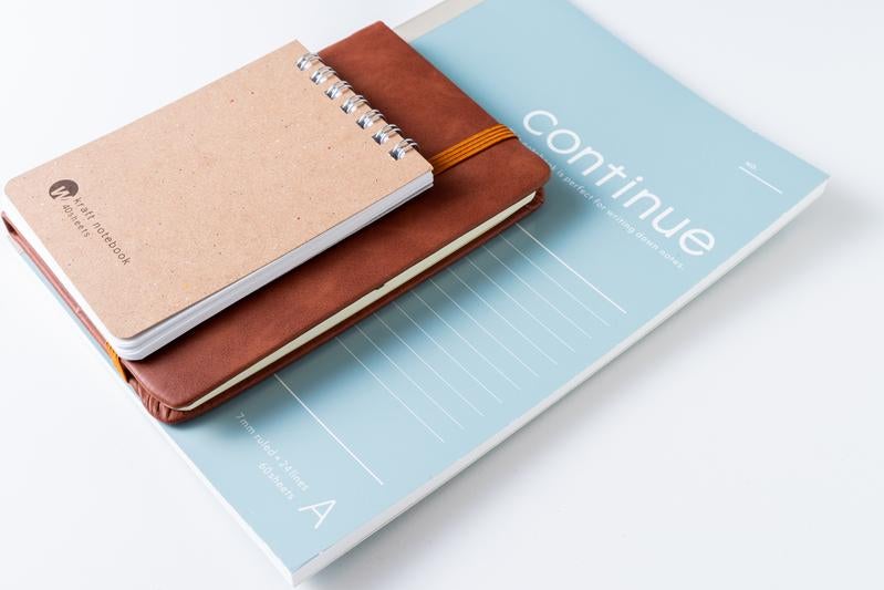 デスクに並べられたリングノートと革製手帳とブルーのファイルの写真