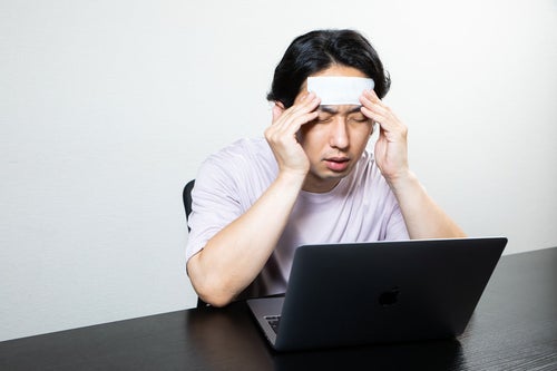 頭痛がひどくてこめかみを抑える男性の写真
