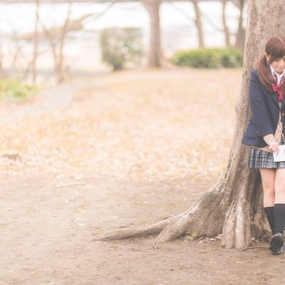 放課後、木陰に隠れて告白のチャンスを伺う女子高生の写真