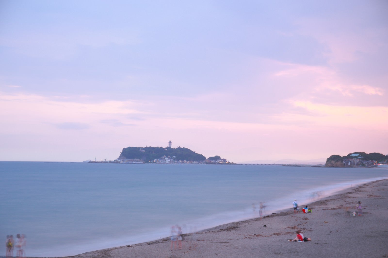 「夕焼けの江ノ島と砂浜で楽しむ人々」の写真