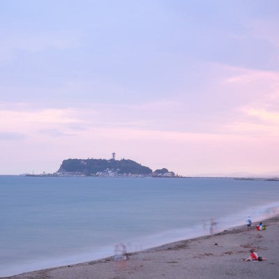 夕焼けの江ノ島と砂浜で楽しむ人々の写真