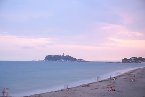 夕焼けの江ノ島と砂浜で楽しむ人々の写真