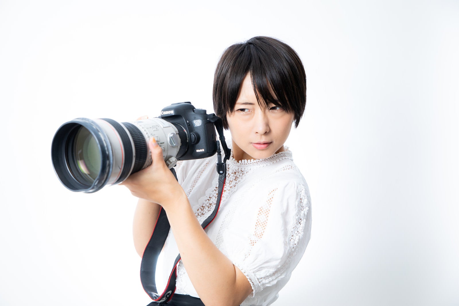 「望遠レンズを装着した一眼レフカメラを重たそうに持つカメラ女子」の写真［モデル：にゃるる］