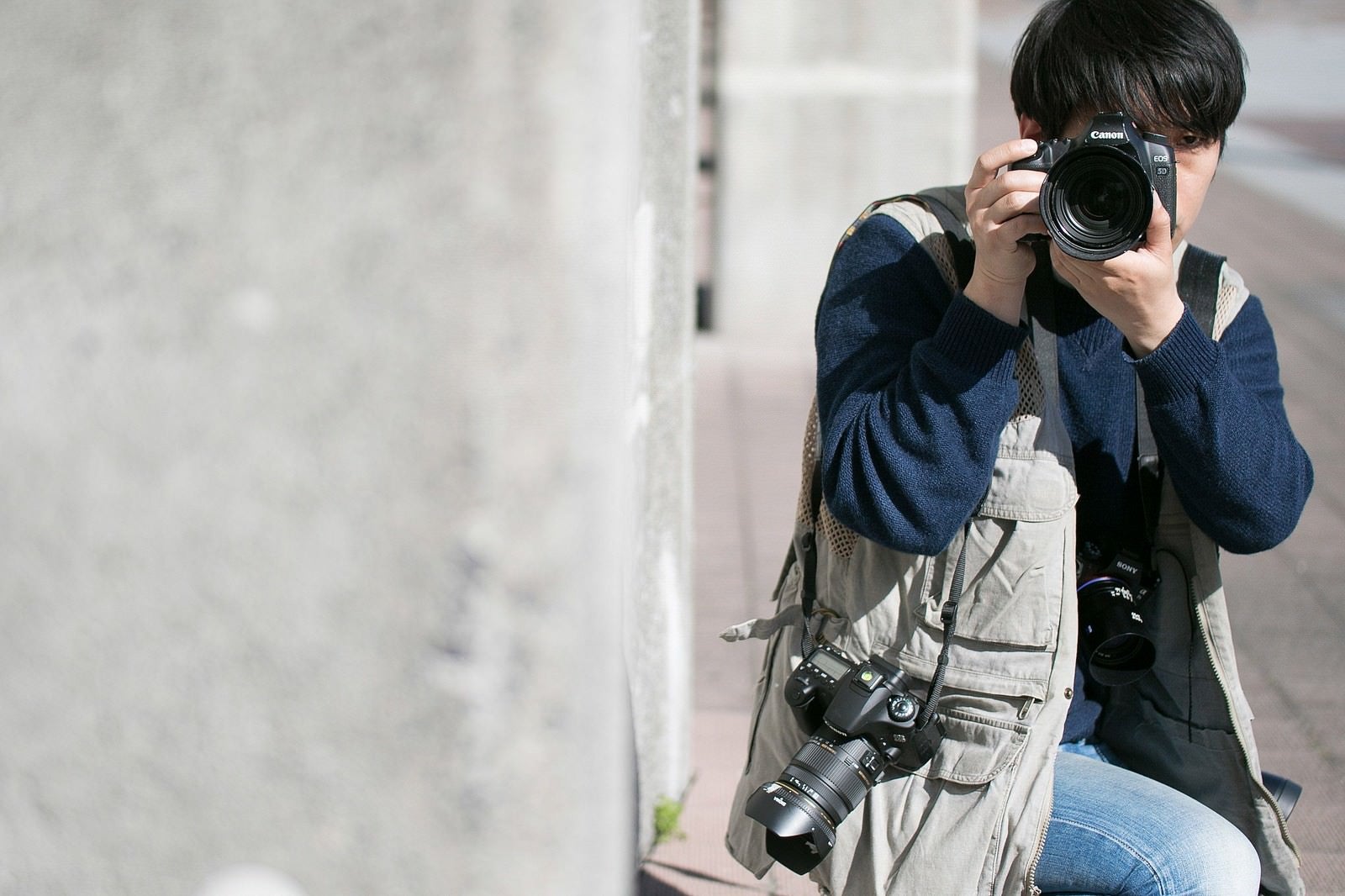 「物陰に隠れて撮影する戦場カメラマン」の写真［モデル：大川竜弥］