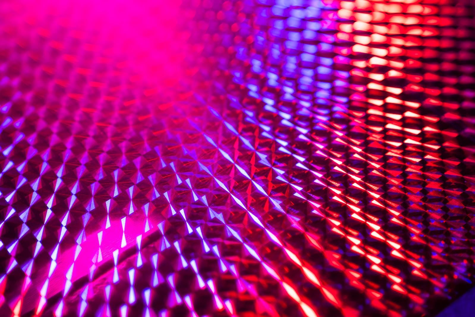 ピンクと青紫に光るホログラムシート表面のダイヤモンド型パターンをマクロ撮影した写真