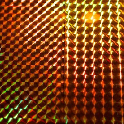 緑と橙色に光るホログラムの立体格子パターンとプリズムの写真