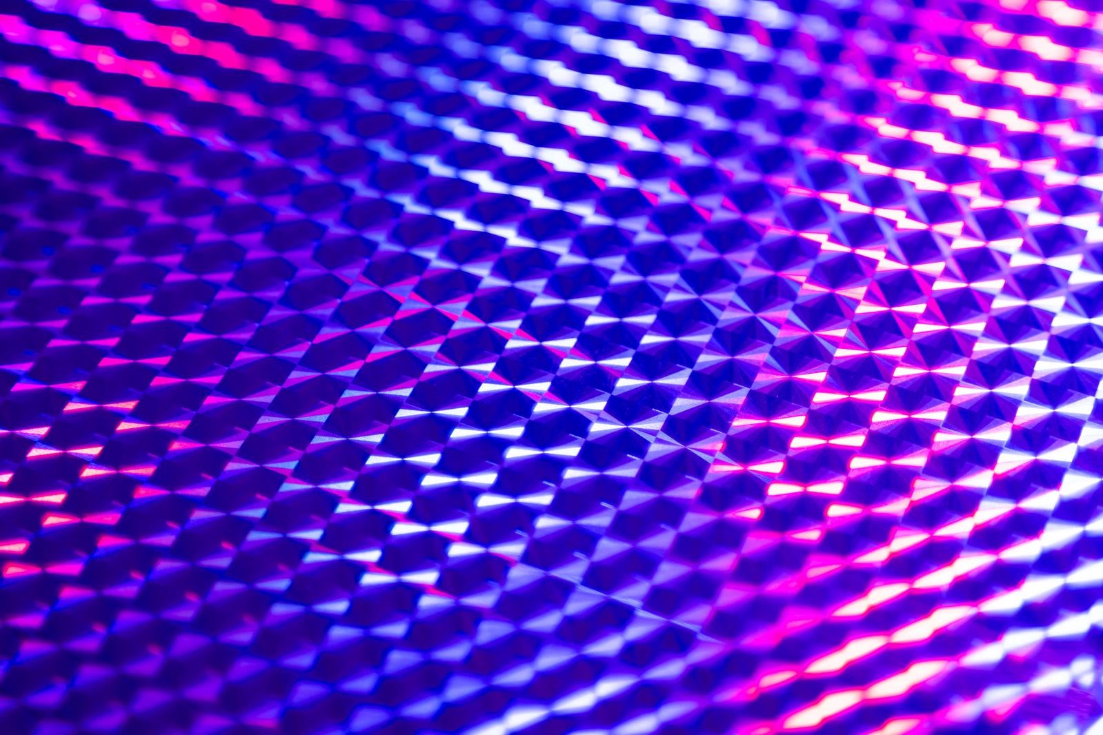 ピンクと紫に光るホログラムシートの格子状の表面を接写した写真