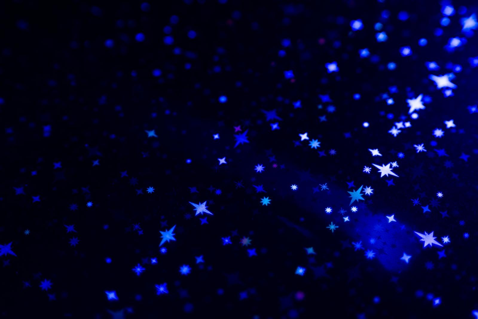 青く輝く星とキラキラした光粒が夜空のように散りばめられた背景