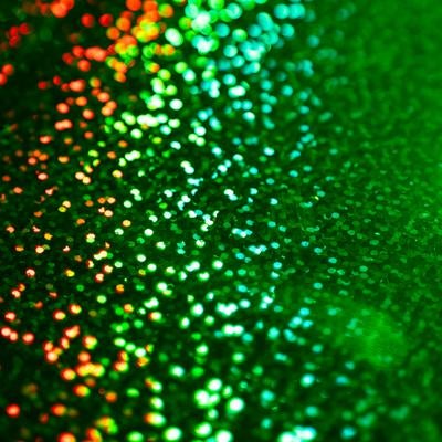 赤からグリーンへグラデーション状に輝く無数のキラキラ粒子の写真