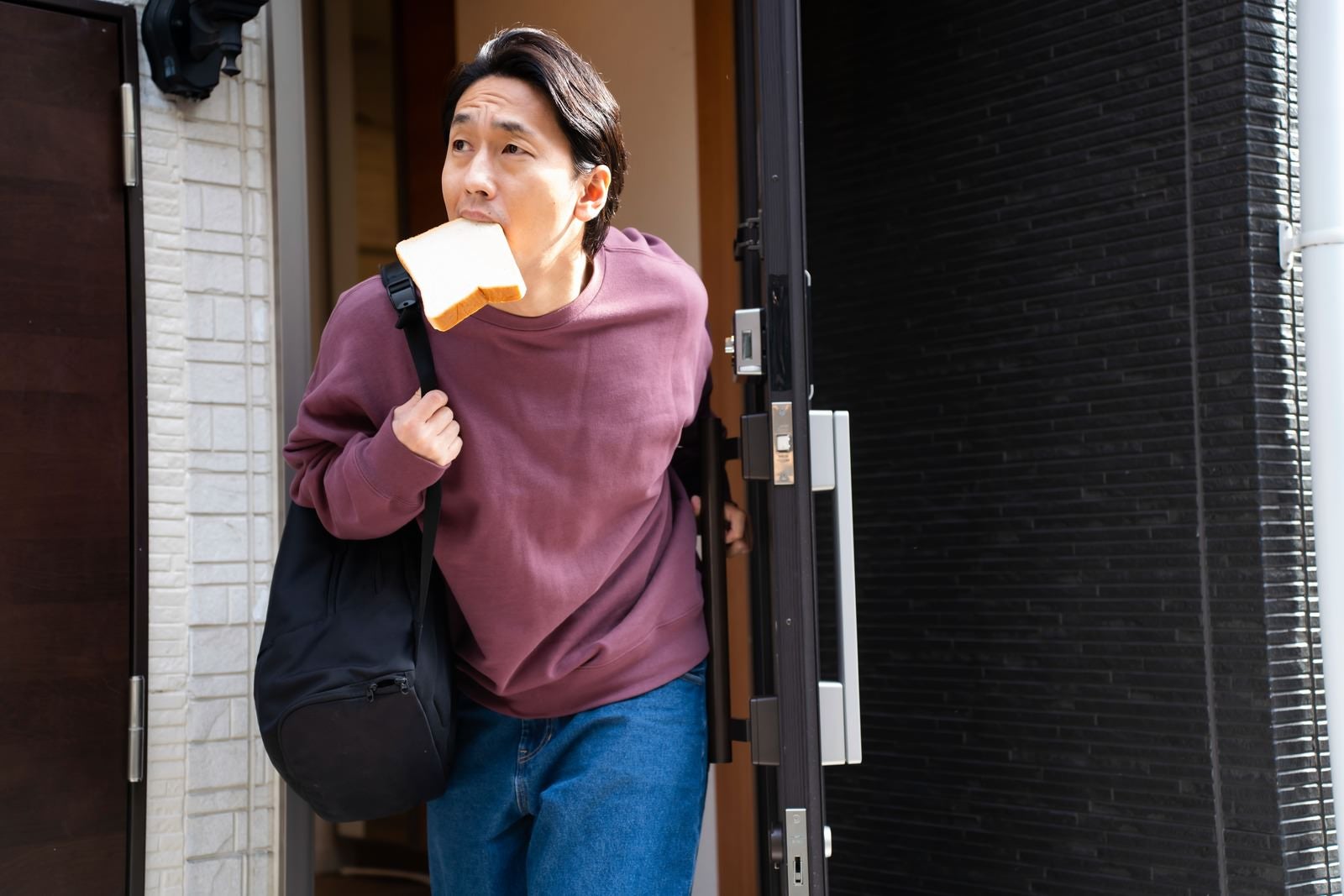 「食パンを咥えながら玄関を出る男性」の写真［モデル：大川竜弥］