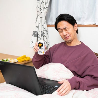 ベッドに入りながらリモート飲みする男性の写真