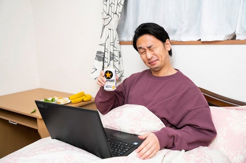 ベッドに入りながらリモート飲みする男性の写真