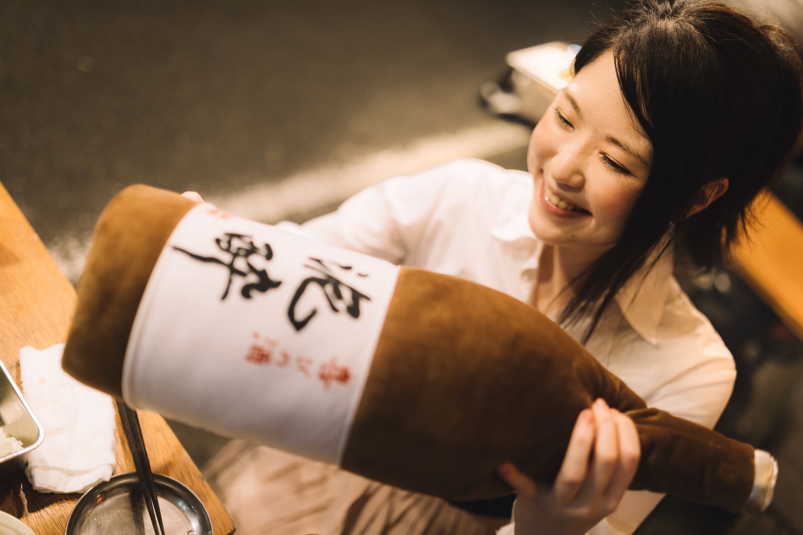 「「泥酔」と書かれた一升瓶の抱き枕をプレゼントされる女性」の写真［モデル：シマヅ］