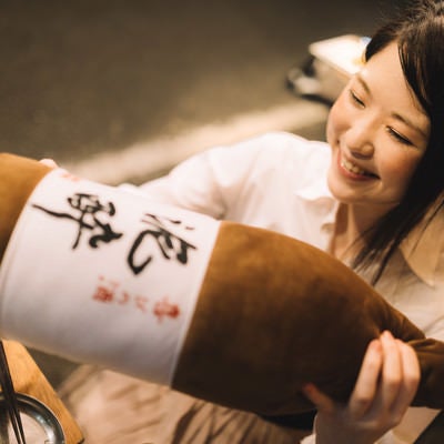 「泥酔」と書かれた一升瓶の抱き枕をプレゼントされる女性の写真
