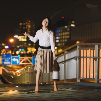 夜間の橋の上で手を広げて立つ女性のポートレートの写真