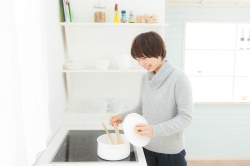 キッチンでスープを温めなおしている女性の写真