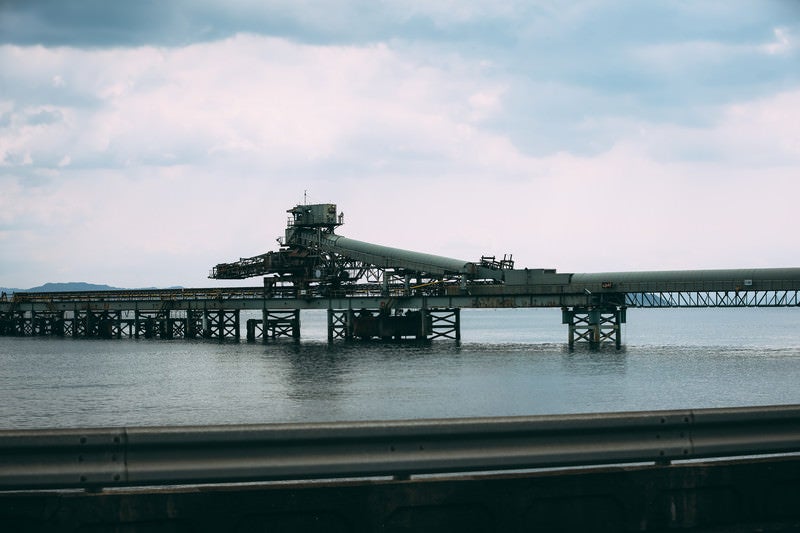 ガードレール越しに見る海上の工場の写真